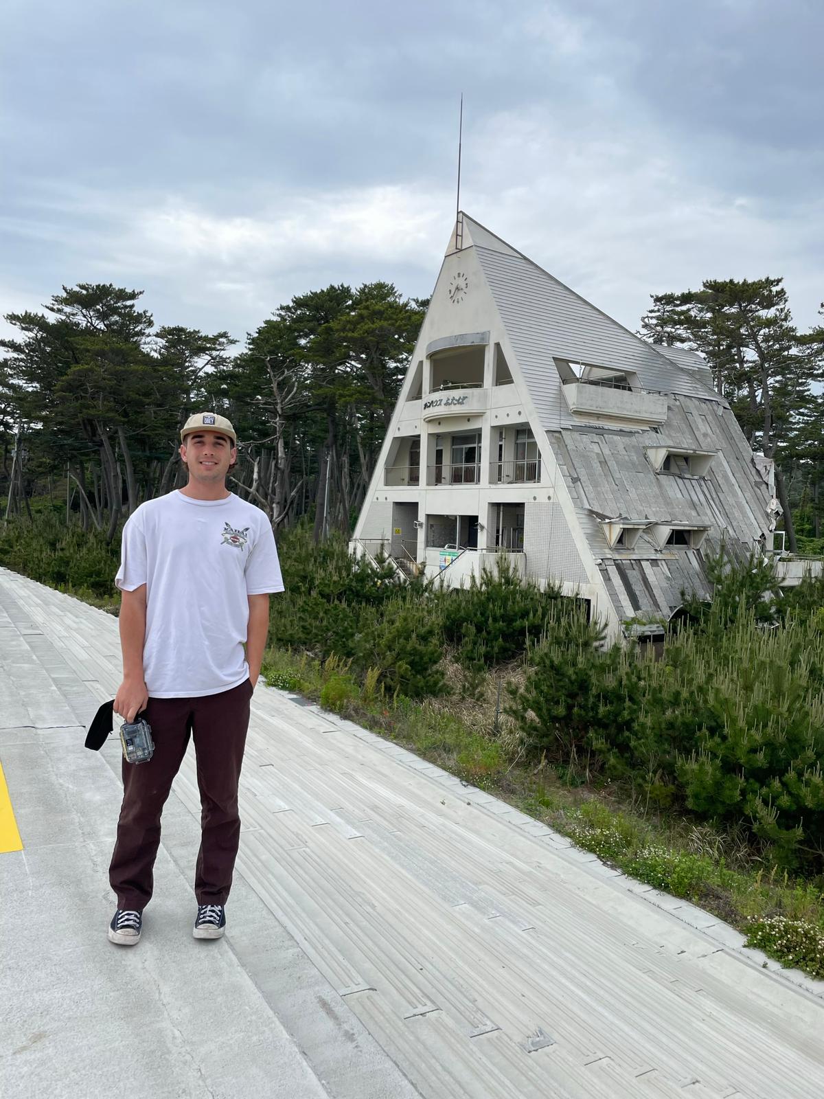 The author standing with a bGeigie on the new seawall in Futaba. Behind me is the destroyed Marine House recreation facility. The tsunami wiped out the first two floors, but some people made it to the third floor and survived.
